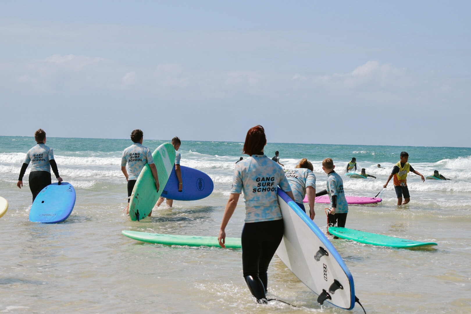 Plusieurs surfeurs de dos vont vers les vagues de Biscarrosse