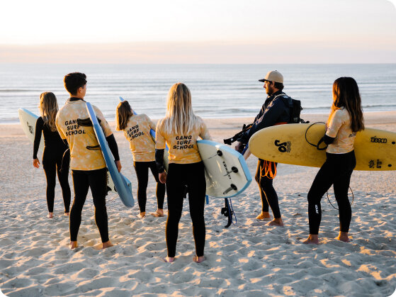 6 surfeurs avec un moniteur sur la plage de Biscarrosse au couché de soleil